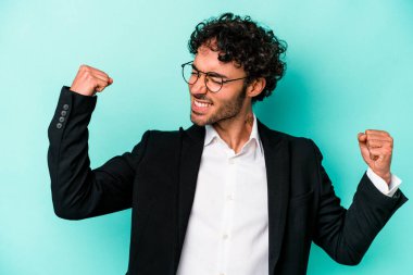 Young caucasian business man isolated on blue background raising fist after a victory, winner concept. clipart