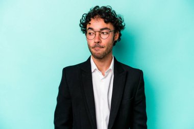 Kafkasyalı genç iş adamı mavi arka planda izole edilmiş, kafası karışmış, şüpheli ve güvensiz hissediyor..