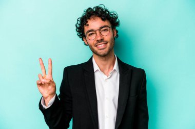 Kafkasyalı genç iş adamı mavi arka planda izole edilmiş neşeli ve kaygısız parmakları olan bir barış sembolü gösteriyor..