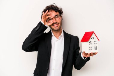 Beyaz arka planda izole edilmiş bir oyuncak evi tutan Kafkasyalı genç bir iş adamı heyecanla bekliyor..