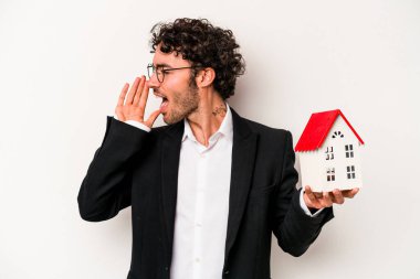 Beyaz arka planda izole edilmiş bir oyuncak evi tutan Kafkasyalı genç bir iş adamı bağırıyor ve avuç içi kadar açık bir ağız tutuyor..