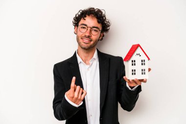 Beyaz arka planda izole edilmiş bir oyuncak evi tutan Kafkasyalı genç bir iş adamı sanki seni davet ediyormuş gibi seni işaret ediyor..