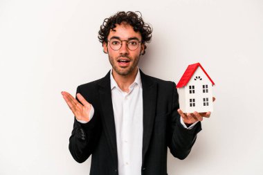 Beyaz arka planda izole edilmiş bir oyuncak evi tutan Kafkasyalı genç iş adamı şaşırdı ve şok oldu..