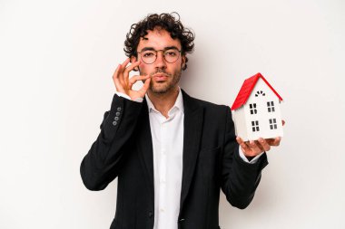 Beyaz arka planda izole edilmiş bir oyuncak evi tutan Kafkasyalı genç bir iş adamı parmakları dudaklarında bir sır saklıyor..