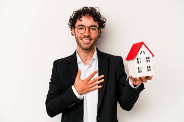 Beyaz arka planda izole edilmiş bir oyuncak evi tutan Kafkasyalı genç iş adamı kahkahalar atıyor..