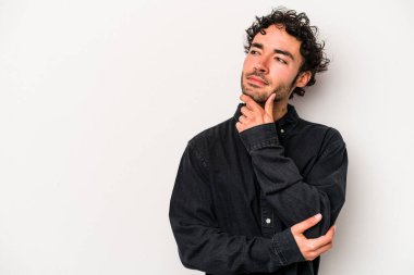 Beyaz arka planda izole edilmiş genç beyaz bir adam şüpheli ve şüpheci bir ifadeyle yana bakıyor..