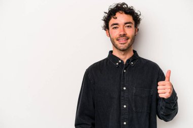 Beyaz arka planda izole edilmiş genç beyaz adam gülümsüyor ve başparmağını kaldırıyor.