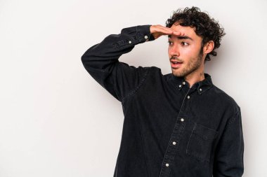 Beyaz arka planda izole edilmiş genç beyaz bir adam uzaklara bakıyor ve elini alnına koyuyor..