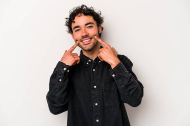 Beyaz arka planda izole edilmiş genç beyaz adam gülümsüyor, parmaklarını ağıza doğrultuyor..