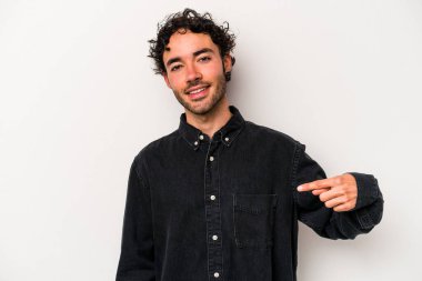 Beyaz arka planda yaşayan beyaz tenli genç bir adam gömlek fotokopi alanını gösteriyor, gururlu ve kendinden emin.