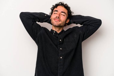 Beyaz arka planda izole olmuş genç beyaz bir adam kendini güvende hissediyor, elleri başının arkasında..