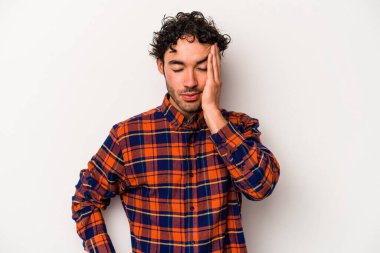 Beyaz arka planda izole edilmiş genç beyaz bir adam yorgun ve uykulu bir şekilde elini başının üstünde tutuyor..