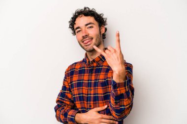 Beyaz arka planda izole edilmiş genç beyaz bir adam parmaklarıyla kaya hareketi gösteriyor.