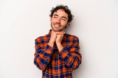 Beyaz arka planda izole genç beyaz adam ellerini çenesinin altında tutuyor, mutlu bir şekilde yana bakıyor..