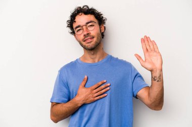 Beyaz arka planda izole edilmiş genç beyaz adam yemin ediyor, elini göğsüne koyuyor..