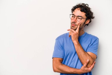 Beyaz arka planda izole edilmiş genç beyaz bir adam şüpheli ve şüpheci bir ifadeyle yana bakıyor..