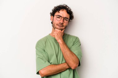 Beyaz arka planda izole edilmiş genç beyaz bir adam şüpheli, belirsiz, seni muayene ediyor..