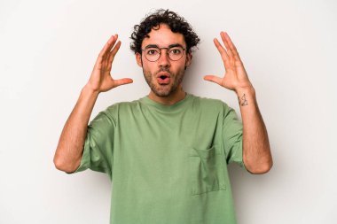 Beyaz arka planda izole olmuş genç beyaz bir adam zaferi veya başarıyı kutluyor, şaşırıyor ve şok oluyor..