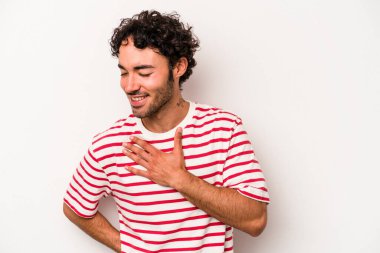 Beyaz arka planda soyutlanmış beyaz tenli genç bir adam gülüyor, elini yüreğine koyuyor, mutluluk kavramını koruyor..