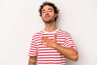 Beyaz arka planda izole edilmiş genç beyaz adam yemin ediyor, elini göğsüne koyuyor..