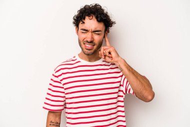 Beyaz arka planda izole edilmiş genç beyaz bir adam parmaklarıyla kulaklarını kapatıyor, gürültülü bir ortam yüzünden stresli ve çaresiz..