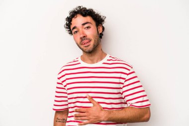 Beyaz arka planda izole edilmiş genç beyaz adam karnına dokunuyor, nazikçe gülümsüyor, yemek yiyor ve tatmin oluyor..