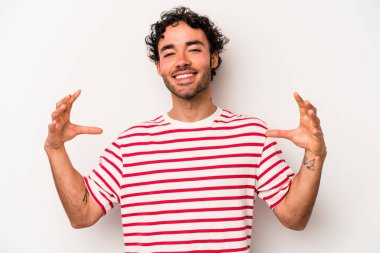 Beyaz arka planda izole edilmiş genç beyaz bir adam elinde avuç içi bir şeyle kameraya sunuyor..