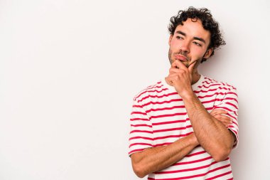 Beyaz arka planda izole edilmiş genç beyaz bir adam şüpheli ve şüpheci bir ifadeyle yana bakıyor..