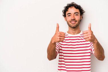Beyaz arka planda izole edilmiş genç beyaz adam gülümsüyor ve başparmağını kaldırıyor.