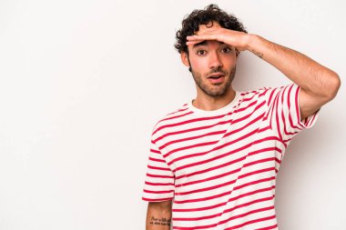 Beyaz arka planda izole edilmiş genç beyaz bir adam uzaklara bakıyor ve elini alnına koyuyor..