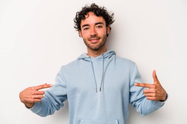 Beyaz arka planda yaşayan beyaz tenli genç bir adam gömlek fotokopi alanını gösteriyor, gururlu ve kendinden emin.