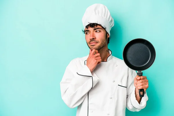 年轻的高加索厨师手里拿着一只被蓝色背景隔离的飞盘 面带怀疑和怀疑的表情侧视着 — 图库照片