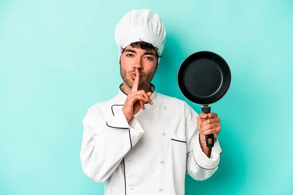 年轻的高加索厨师手持被蓝色背景隔离的飞行锅 保守秘密或要求沉默 — 图库照片