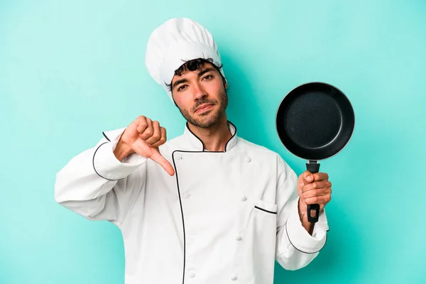 年轻的高加索厨师拿着被蓝色背景隔离的飞盘 表现出不喜欢的姿态 大姆指朝下 不同意的概念 — 图库照片