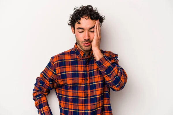 Beyaz arka planda izole edilmiş genç beyaz bir adam yorgun ve uykulu bir şekilde elini başının üstünde tutuyor..