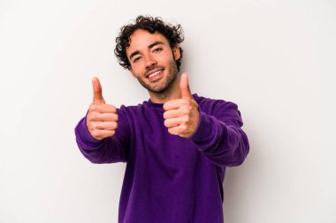 Beyaz arka planda izole edilmiş genç beyaz bir adam iki parmağını da kaldırıyor, gülümsüyor ve kendinden emin..