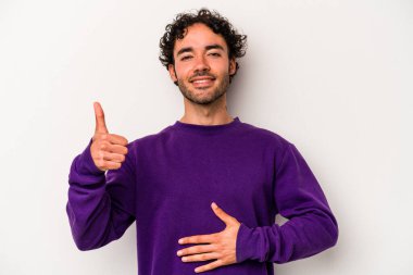 Beyaz arka planda izole edilmiş genç beyaz adam karnına dokunuyor, nazikçe gülümsüyor, yemek yiyor ve tatmin oluyor..