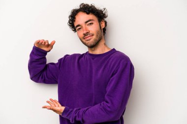 Beyaz arka planda izole edilmiş genç beyaz bir adam işaret parmaklarıyla küçük bir şey tutuyor, gülümsüyor ve kendinden emin..