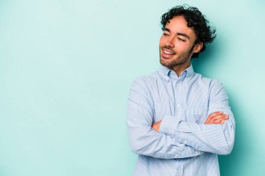 Beyaz arka planda izole edilmiş genç beyaz adam kollarını kavuşturarak gülümsüyor..