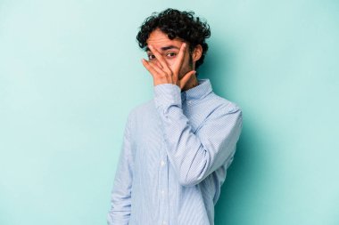 Beyaz arka planda izole edilmiş genç beyaz bir adam kameraya parmaklarıyla göz kırpıyor, yüzünü kapatmaktan utanıyor..