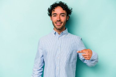 Beyaz arka planda yaşayan beyaz tenli genç bir adam gömlek fotokopi alanını gösteriyor, gururlu ve kendinden emin.