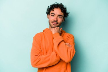 Beyaz arka planda izole olmuş genç beyaz bir adam gülümsüyor ve kendinden emin, çenesine elleriyle dokunuyor..