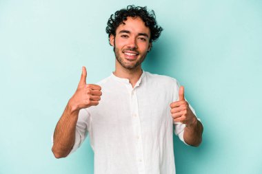 Beyaz arka planda izole edilmiş genç beyaz bir adam iki parmağını da kaldırıyor, gülümsüyor ve kendinden emin..