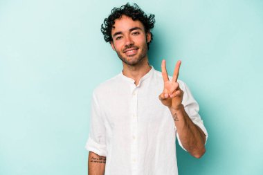 Beyaz arka planda izole edilmiş genç beyaz bir adam zafer işareti gösteriyor ve gülümsüyor..