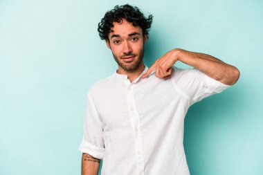 Beyaz arka planda yaşayan beyaz tenli genç bir adam gömlek fotokopi alanını gösteriyor, gururlu ve kendinden emin.