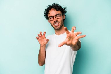 Beyaz arka planda izole edilmiş genç beyaz bir adam pençelerini kedi taklidi yaparken gösteriyor, agresif bir hareket..