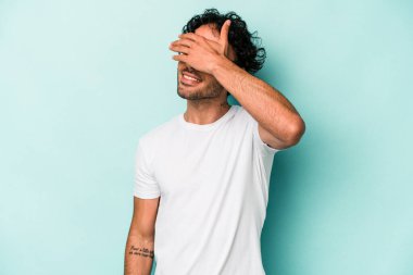 Beyaz arka planda soyutlanmış beyaz tenli genç bir adam elleriyle gözlerini kapatıyor, geniş bir gülümsemeyle bir sürpriz bekliyor..