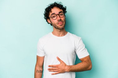 Beyaz arka planda izole edilmiş genç beyaz adam karnına dokunuyor, nazikçe gülümsüyor, yemek yiyor ve tatmin oluyor..