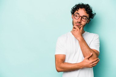 Beyaz arka planda izole edilmiş genç beyaz bir adam şüpheli ve şüpheci bir ifadeyle yana bakıyor..