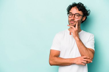 Beyaz arka planda izole edilmiş genç beyaz bir adam şüpheli ve şüpheci bir ifadeyle yana bakıyor..